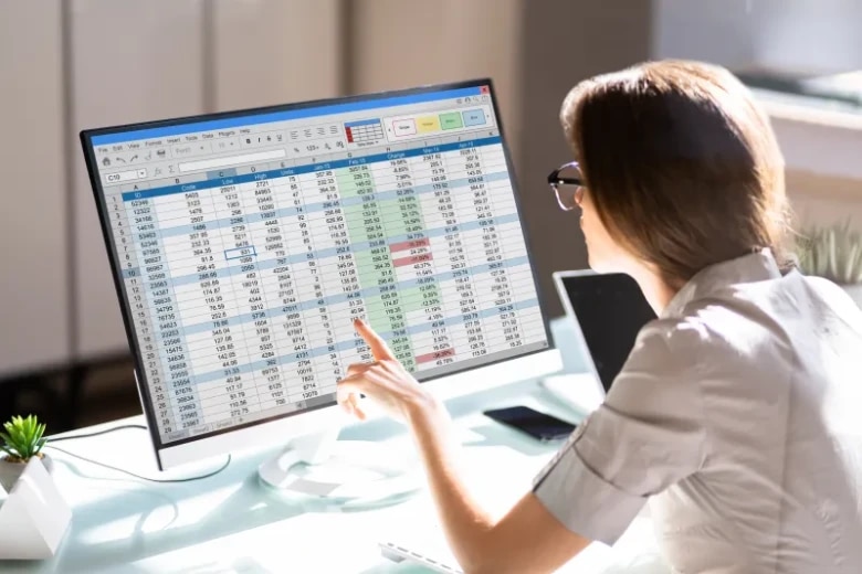 An individual reviews financial data and performance metrics displayed on a computer monitor. Tabular data, calculations, and highlighted values support analysis, reporting, risk assessment, and data-driven decision-making in financial services operations.