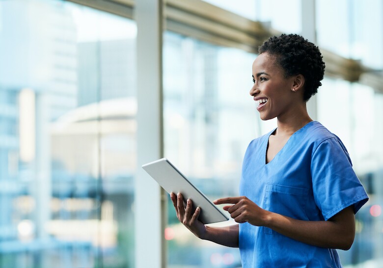 smiling nurse using tablet in hospital hallway