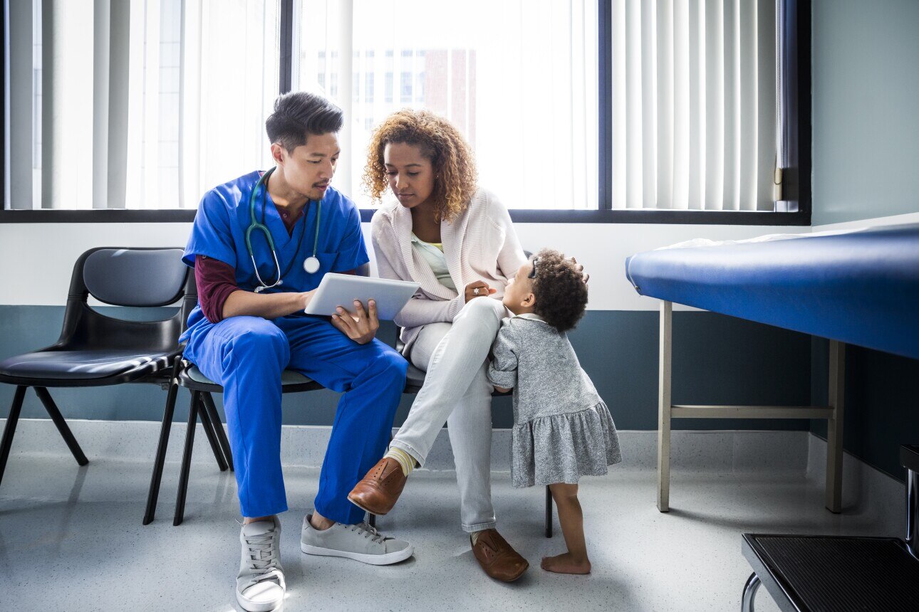 Male nurse showing digital tablet to mother with toddler in hospital