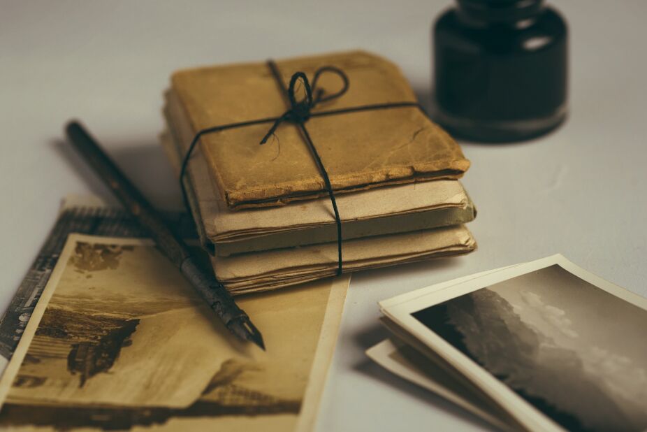 fountain pen and bottle of black ink next to a bundle of aged letters and sepia-tone pictures