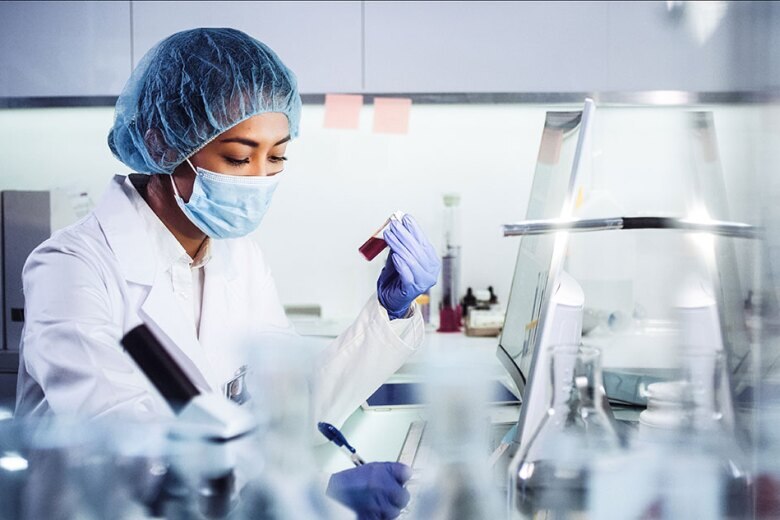 lab tech holding  a vial of liquid and taking notes