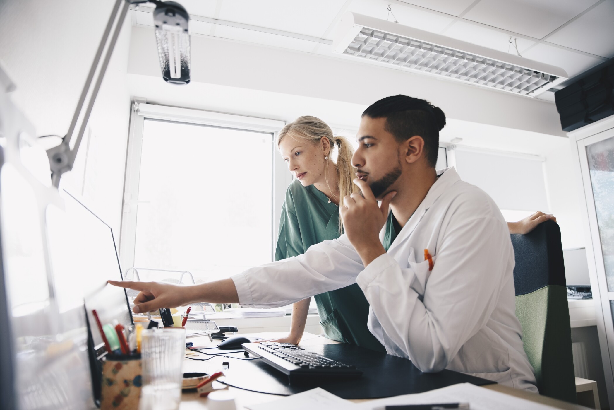 Young male doctor pointing at computer monitor to female nurse in office