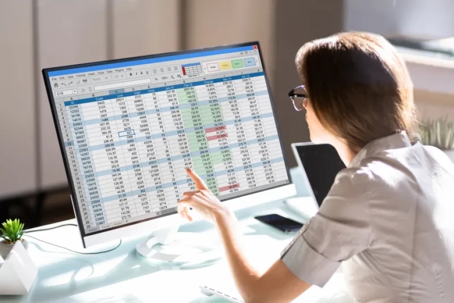 An individual reviews financial data and performance metrics displayed on a computer monitor. Tabular data, calculations, and highlighted values support analysis, reporting, risk assessment, and data-driven decision-making in financial services operations.