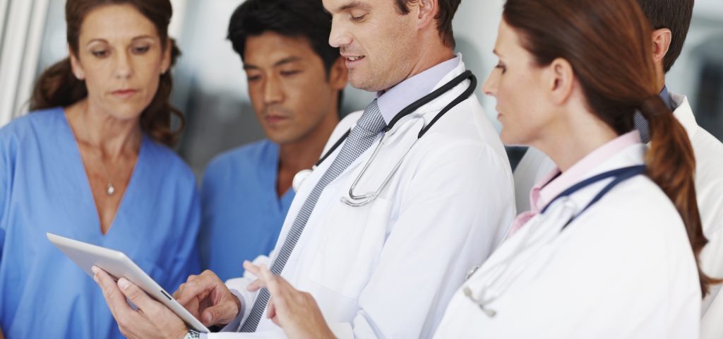 a care team of doctors and nurses looking at information on a tablet