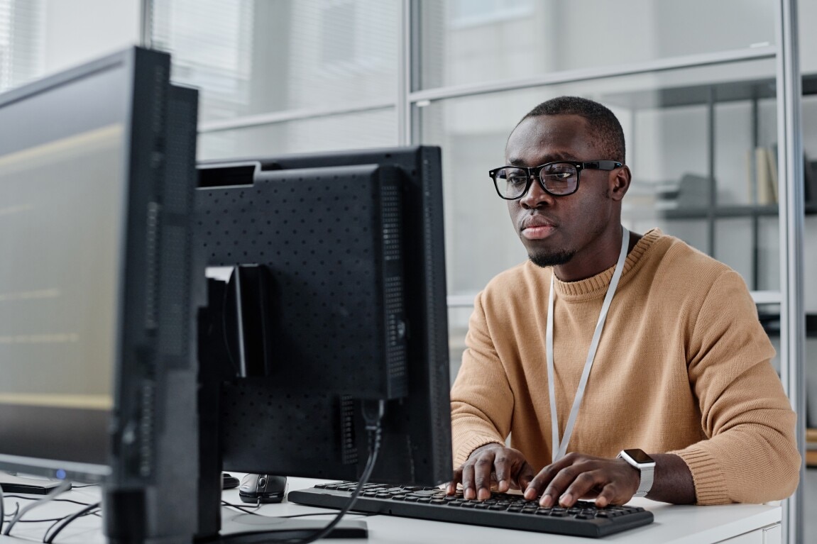 Young black software engineer wearing eyeglasses and concentrating on his computer screen