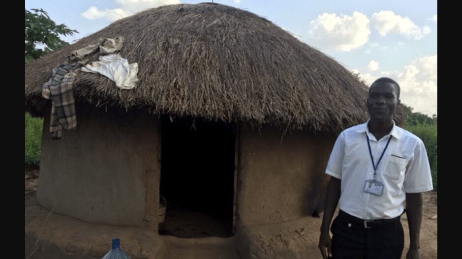 B. DeBoe in front of hut with straw roof