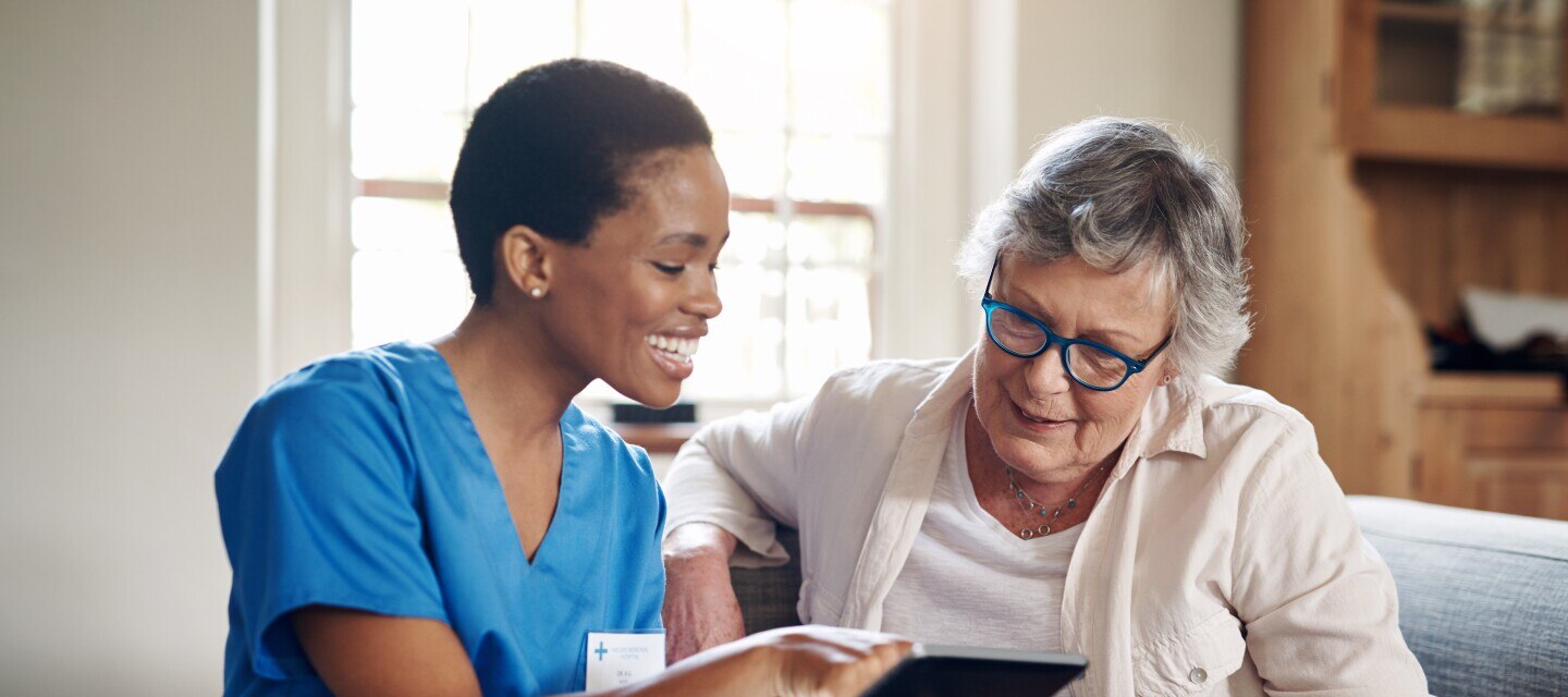 Shot of a senior woman using a digital tablet with a nurse on the sofa at home