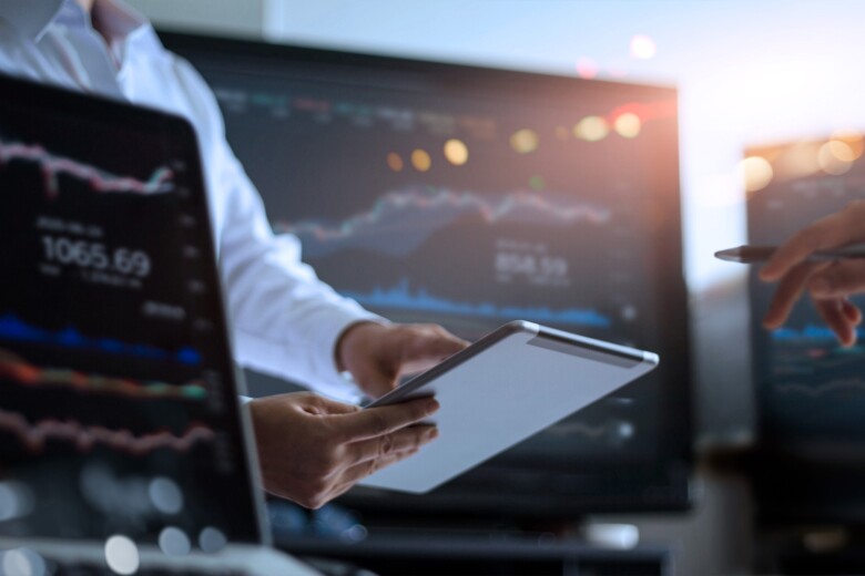 Businessman using tablet for analyzing data stock market in monitoring room with team pointing on the data presented in the chart on screen
