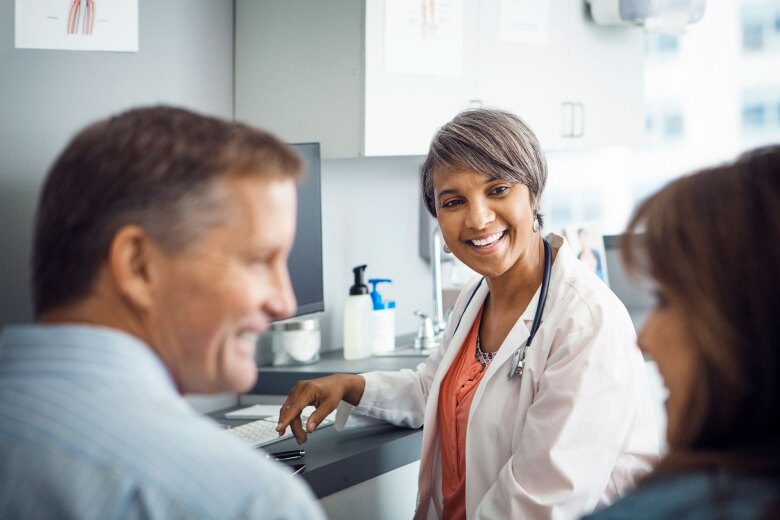 Happy female doctor looking at couple in clinic