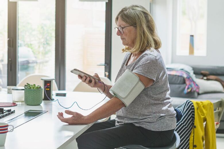 Patient Woman at home checking blood pressure with medical device - healthcare