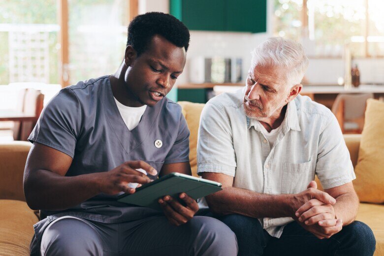 Nurse, elderly man and talk with tablet on sofa for healthcare, communication or consultation it home