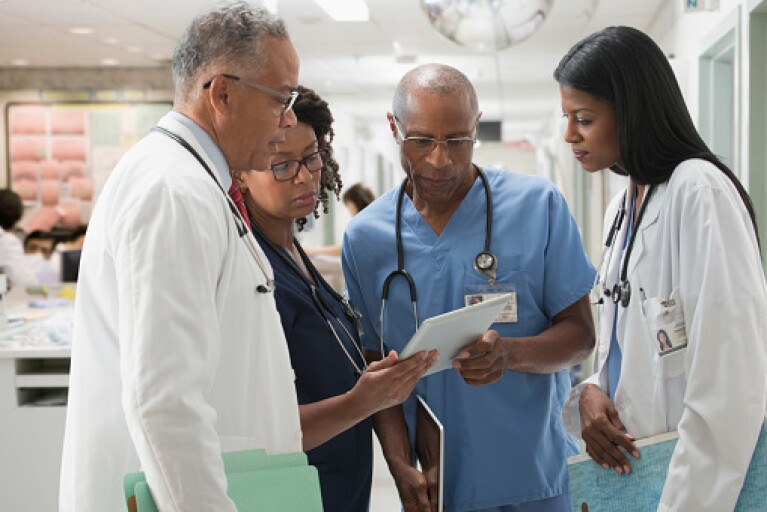 Four doctors reviewing a patient's electronic medical record on a tablet.