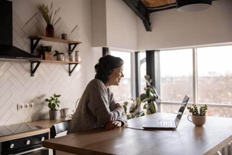 happy woman video chatting on laptop in kitchen