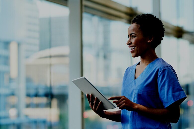 smiling nurse using a tablet by a wall of windows