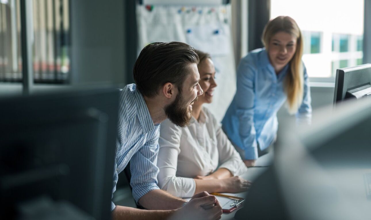 Three office employees sitting at desk smiling