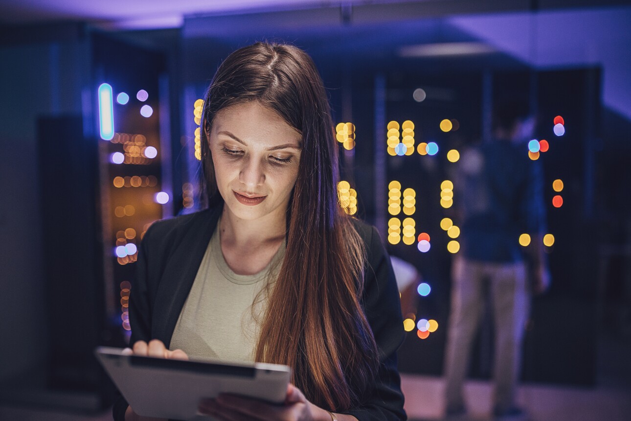 Female maintenance engineer examining data on digital tablet in server room.