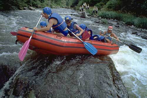 group of people stranded in a raft on a rock in the middle of a river while white water rafting