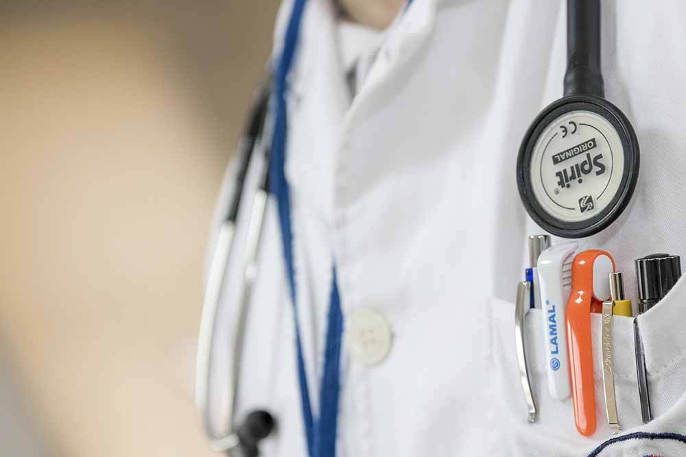 white doctor coat with stethoscope and pocket full of pens