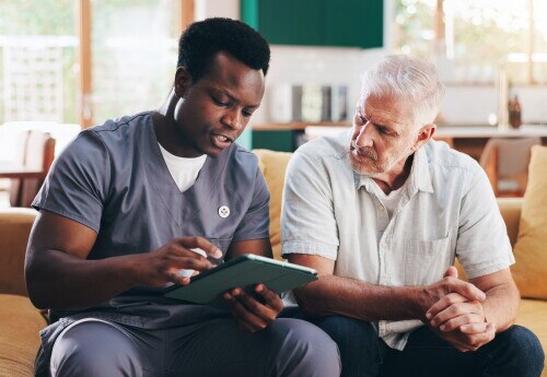 Nurse, elderly man and talk with tablet on sofa for healthcare, communication or consultation it home