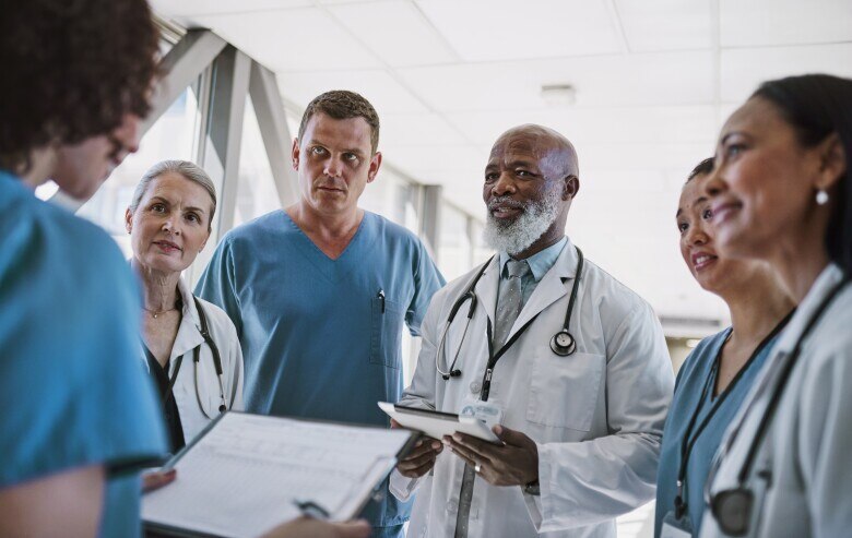 Senior doctor holding clipboard, smiling and listening to nurse talking, together with medical team in hospital