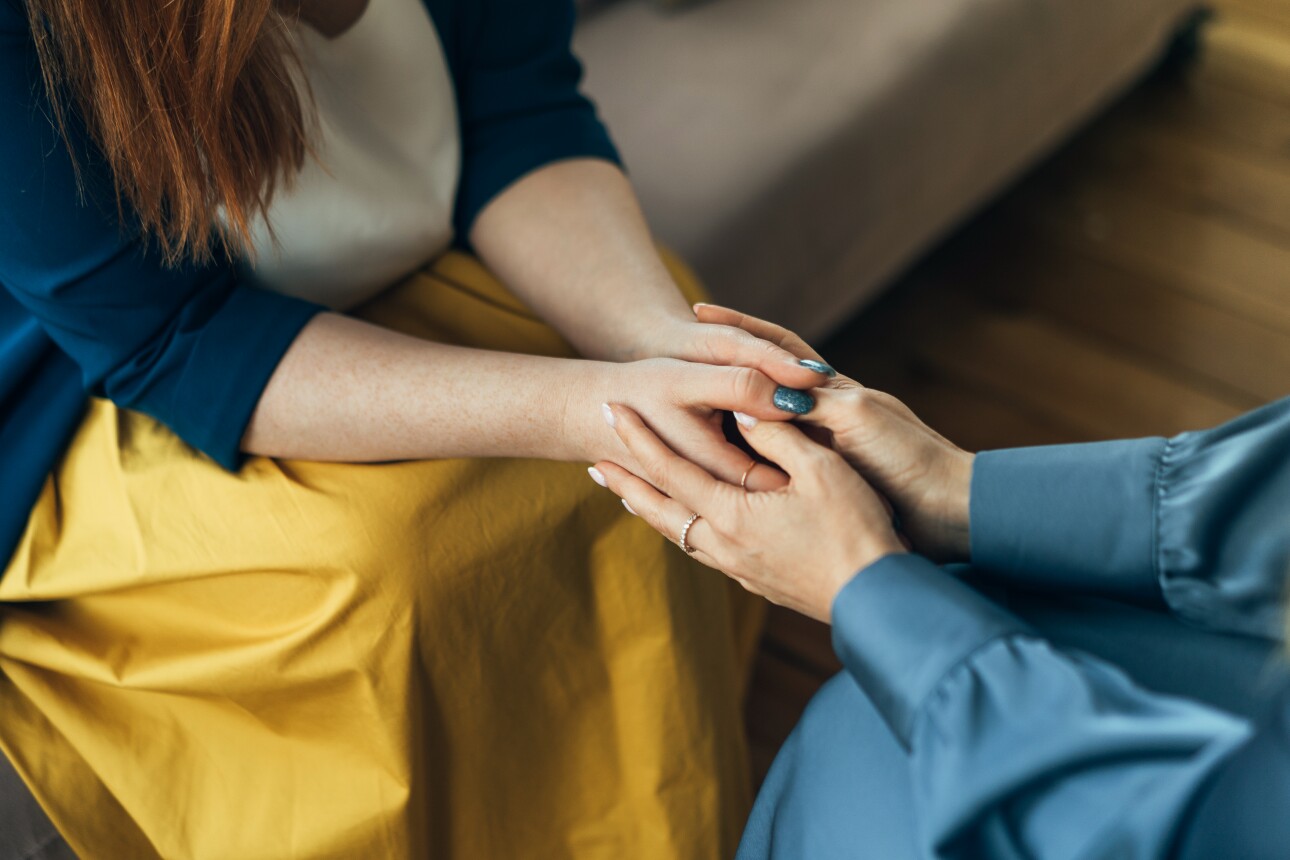 Two women sitting and talking while holding hands.