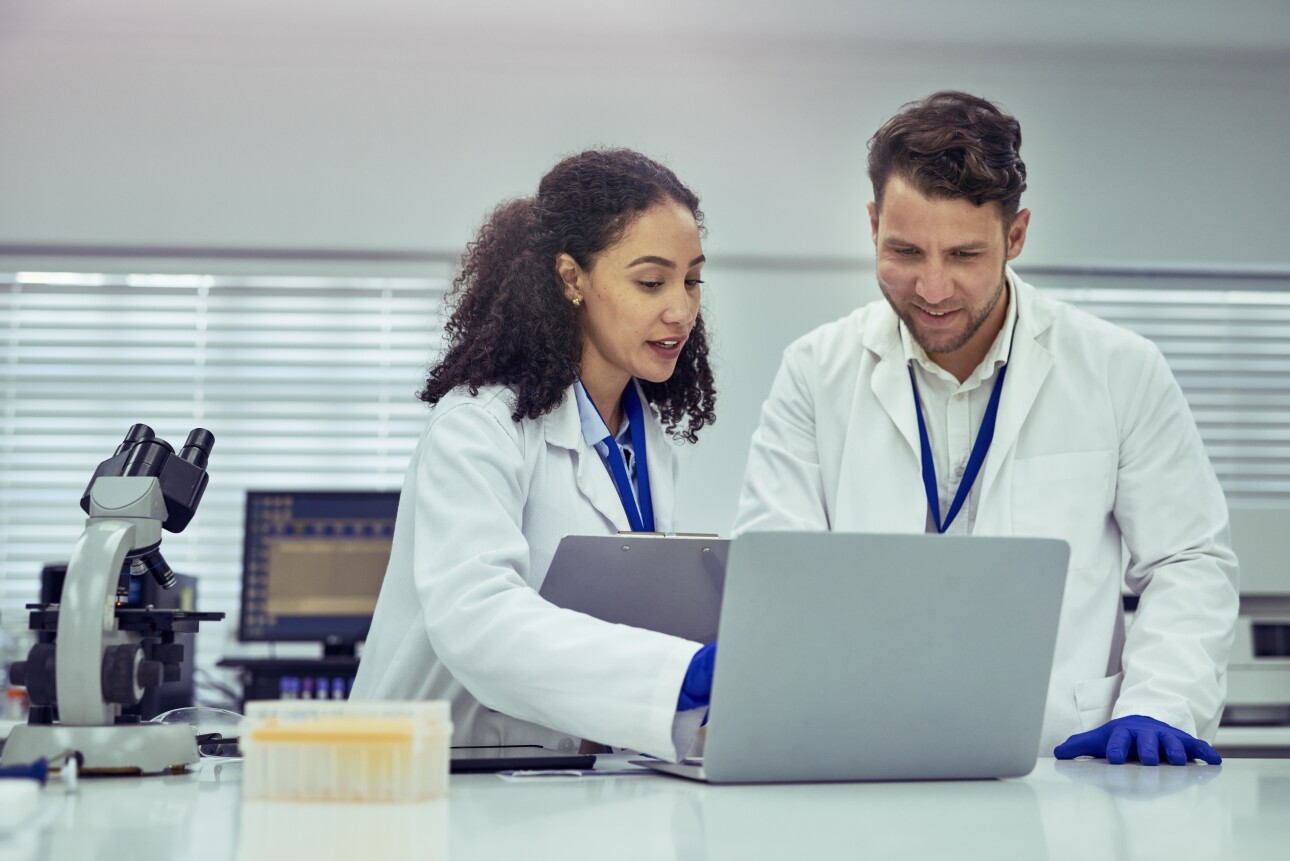 Female scientist and male colleague smiling and discussing work on laptop in laboratory