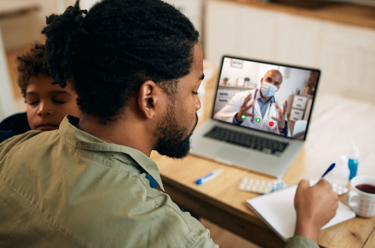 father holding young son while on a telehealth call with the peditrician